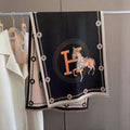 Full view of oversized black soft luxury shawl with ivory equestrian horse and border and orange letter medallion print