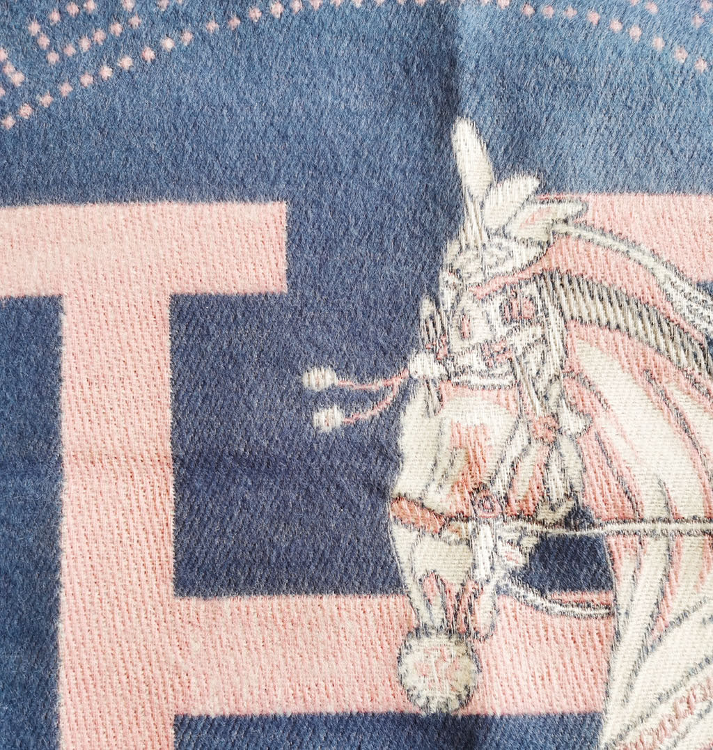 Close-up of luxury blue scarf displaying jacquard horse print and cashmere-feel fabric detail