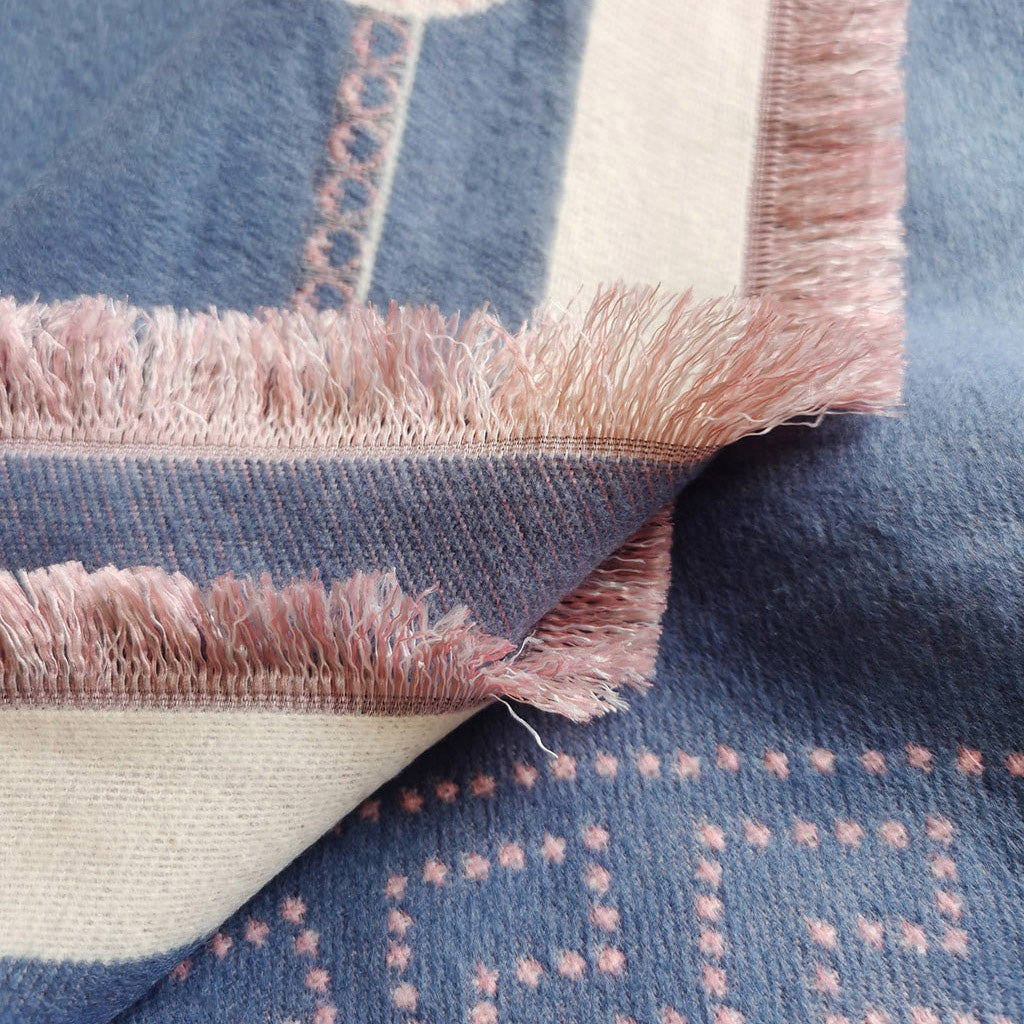 Close-up of luxury blue scarf showing soft pink fringe tassel edge and cashmere-feel jacquard weave detail