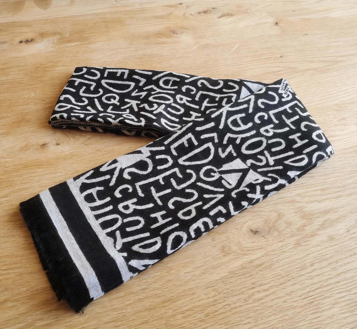 Large size black and white alphabet print scarf is displayed on light background. The cashmere-feel winter neck scarf is folded as a Men's scarf styling method
