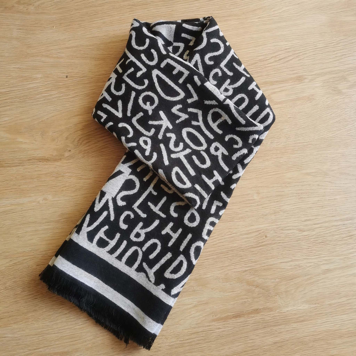 Black and white letters pattern winter scarf folded on light background as a Men's scarf styling method. It shows cashmere-feel fabric with high-quality.