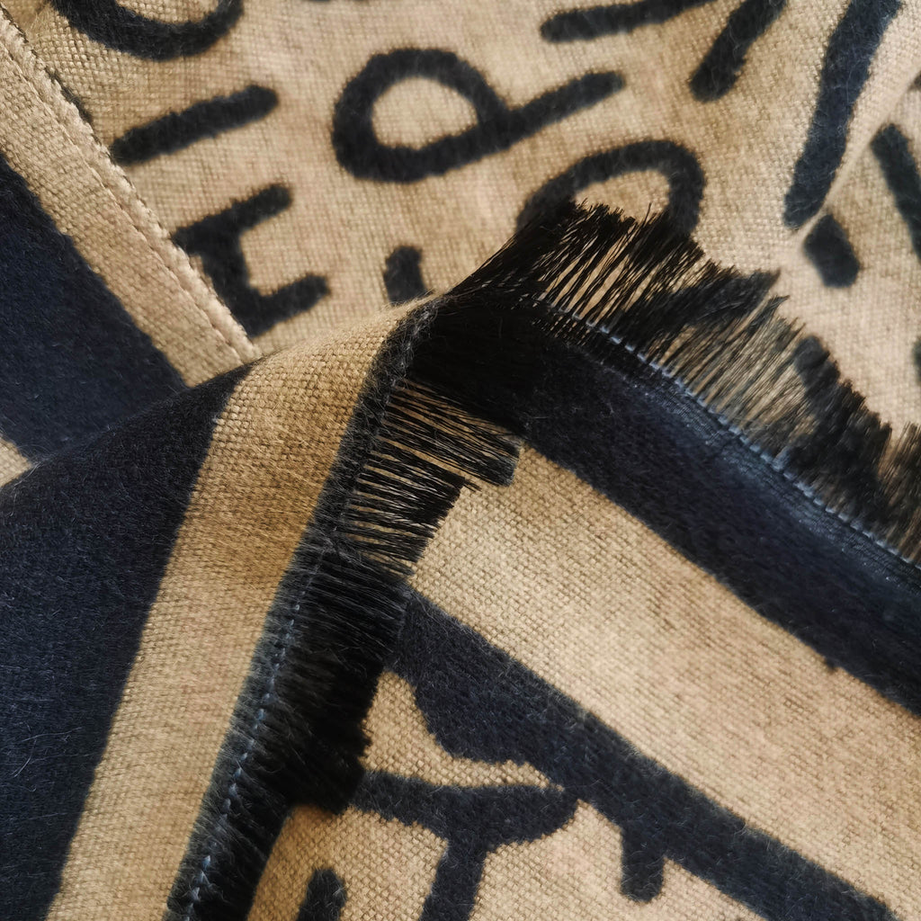 Close-up of fringe detail and cashmere-feel fabric texture on black and camel letter pattern winter scarf. Clean stitching throughout for a quality feel.