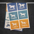 Full view of a soft cashmere-feel winter scarf with blue and yellow panel and horse print hanging on rod. This unisex fashion scarf is large size, approx. width 65 cm, length 180 cm and weight 330g