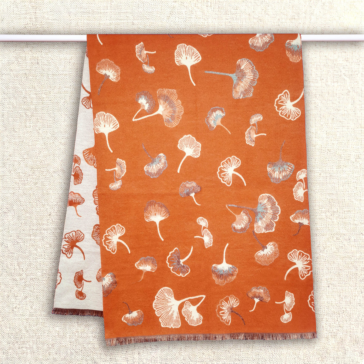 An orange women scarf with floral pattern is hanging on clothing rack. It is a large size scarf. The cashmere-feel fabric is very soft, warm and with high-quality workmanship.