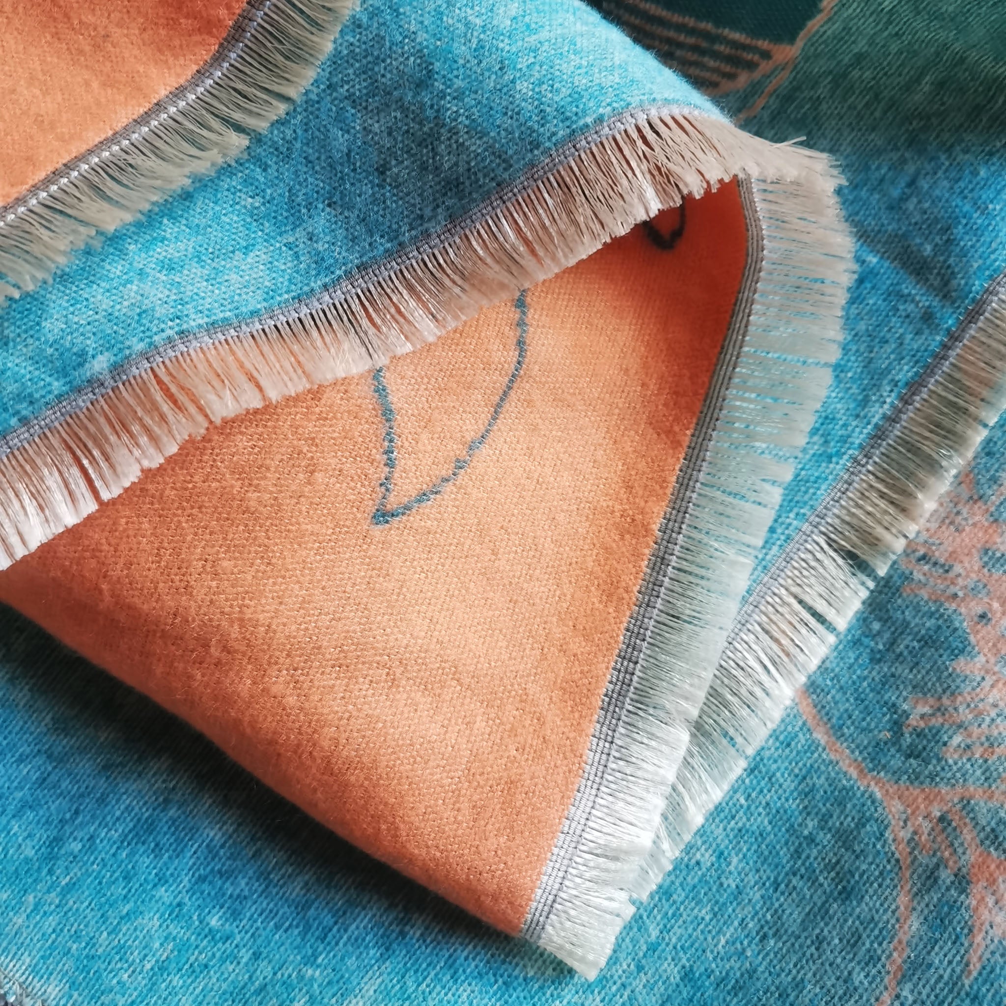 folded women winter scarf showing teal and orange cashmere-feel texture with natural fringe edge detail