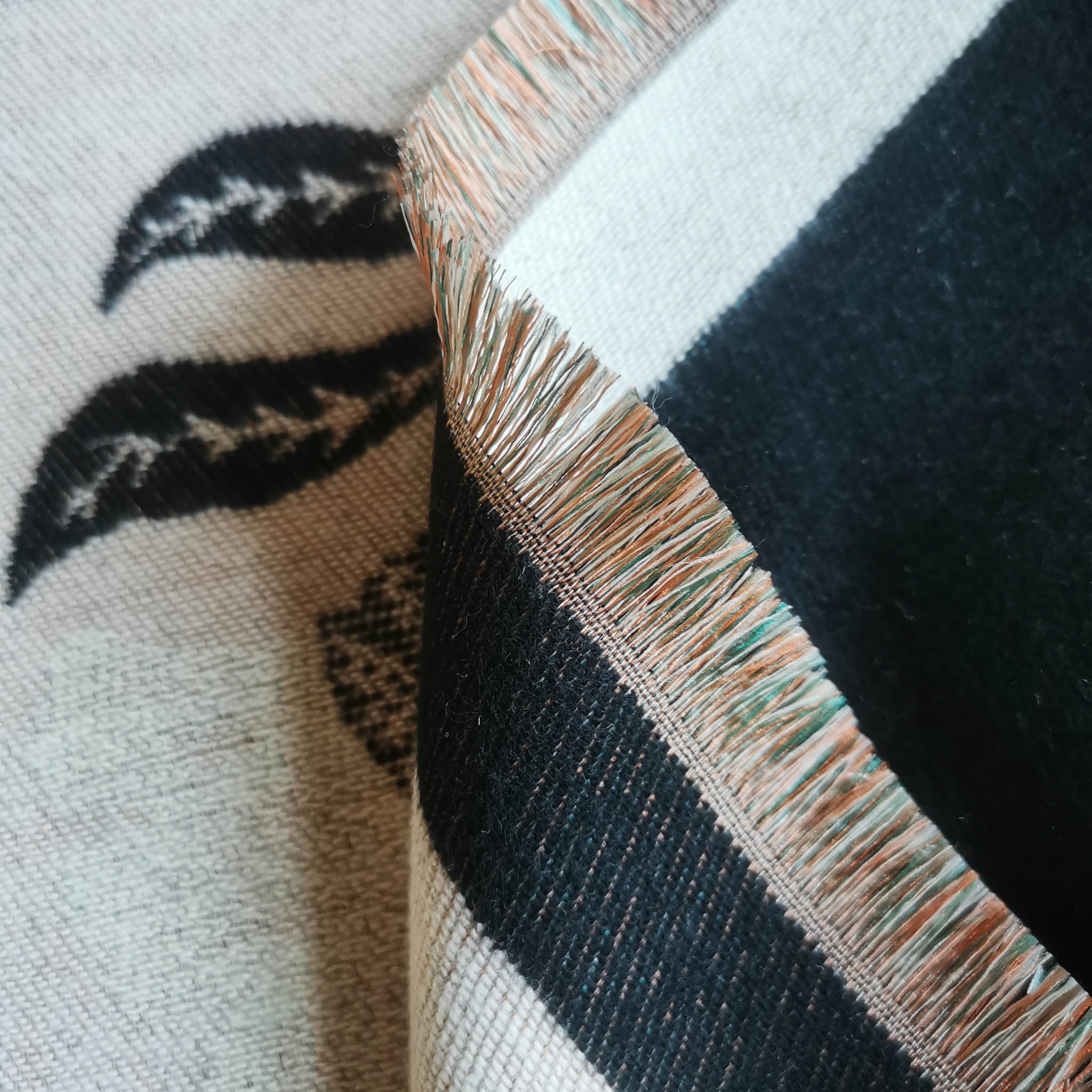 Close-up of multi-tone natural fringe edge of cashmere-feel women scarf with black leaf detail on cream background
