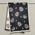 Floral black women winter scarf cashmere-feel fabric hanging on display rail showing scattered fan-shaped flower and leaf pattern with cream border and fringe edges. The large size is enough to wrap as a fashion shawl