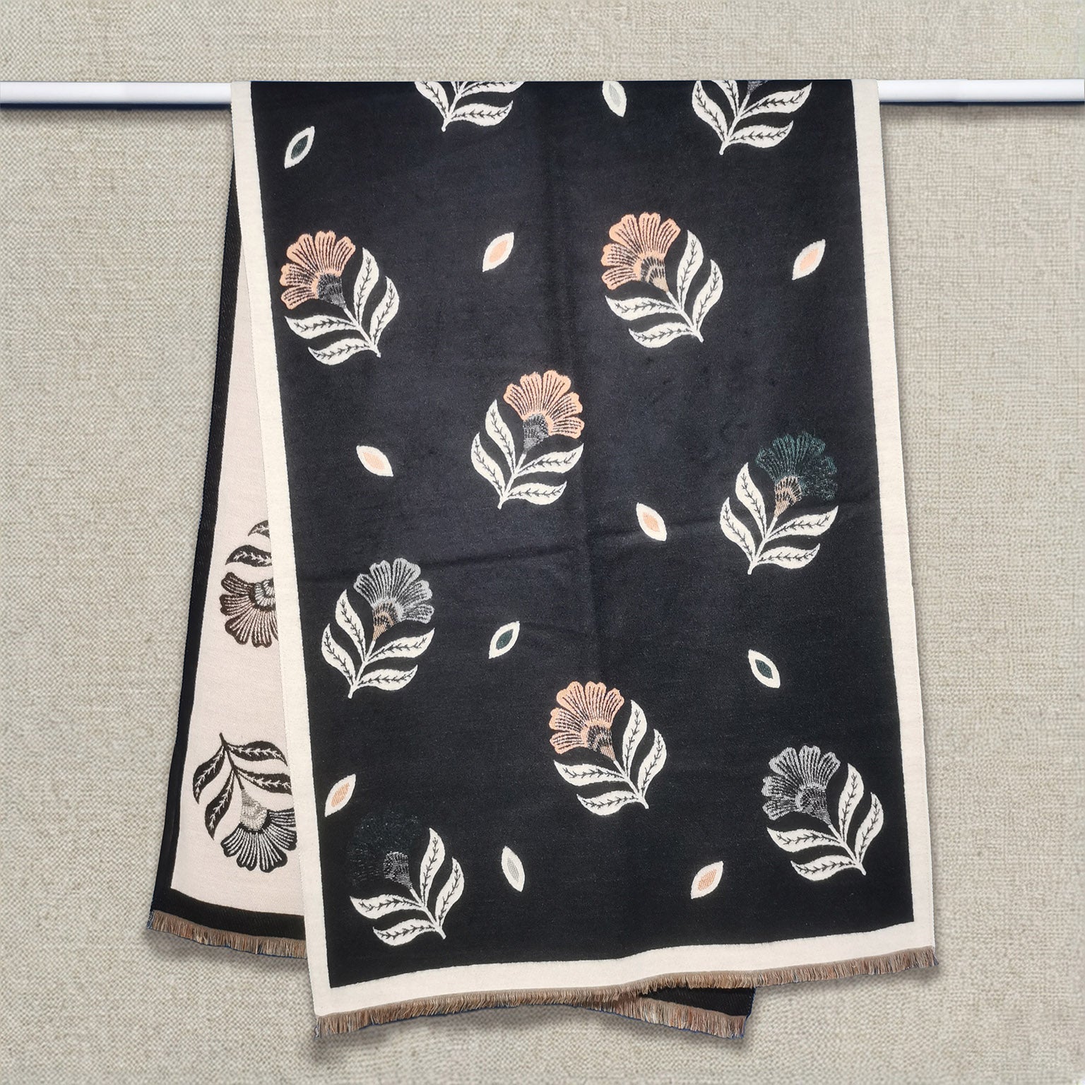 Floral black women winter scarf cashmere-feel fabric hanging on display rail showing scattered fan-shaped flower and leaf pattern with cream border and fringe edges. The large size is enough to wrap as a fashion shawl