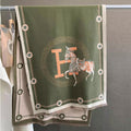 oliver green elegant horse print winter scarf with orange letter and ivory border hanging on display rack