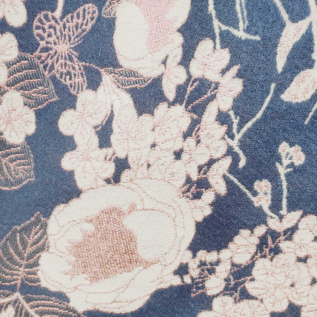 Close-up detail of jacquard scarf fabric showing blush pink floral bird and butterfly on dusty blue background. The details show the winter woman scarf is crafted with high-end workmanship