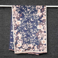 Full view of cashmere-feel winter women scarf in dusty blue hanging on display rail showing birds on branches and butterflies pattern with cream border and pink fringe