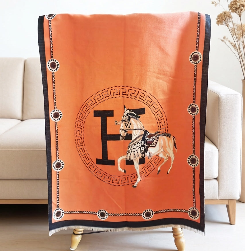 Orange luxury equestrian print shawl with black trim draped over a chair, horse and letter medallion design