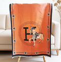 Orange luxury equestrian print shawl with black trim draped over a chair, horse and letter medallion design