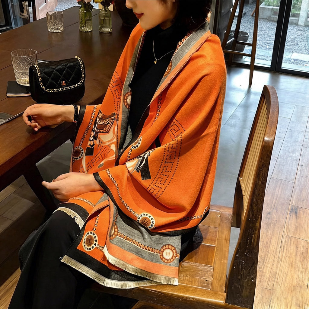 Woman seated wearing luxury orange equestrian wrap scarf with horse print and black border
