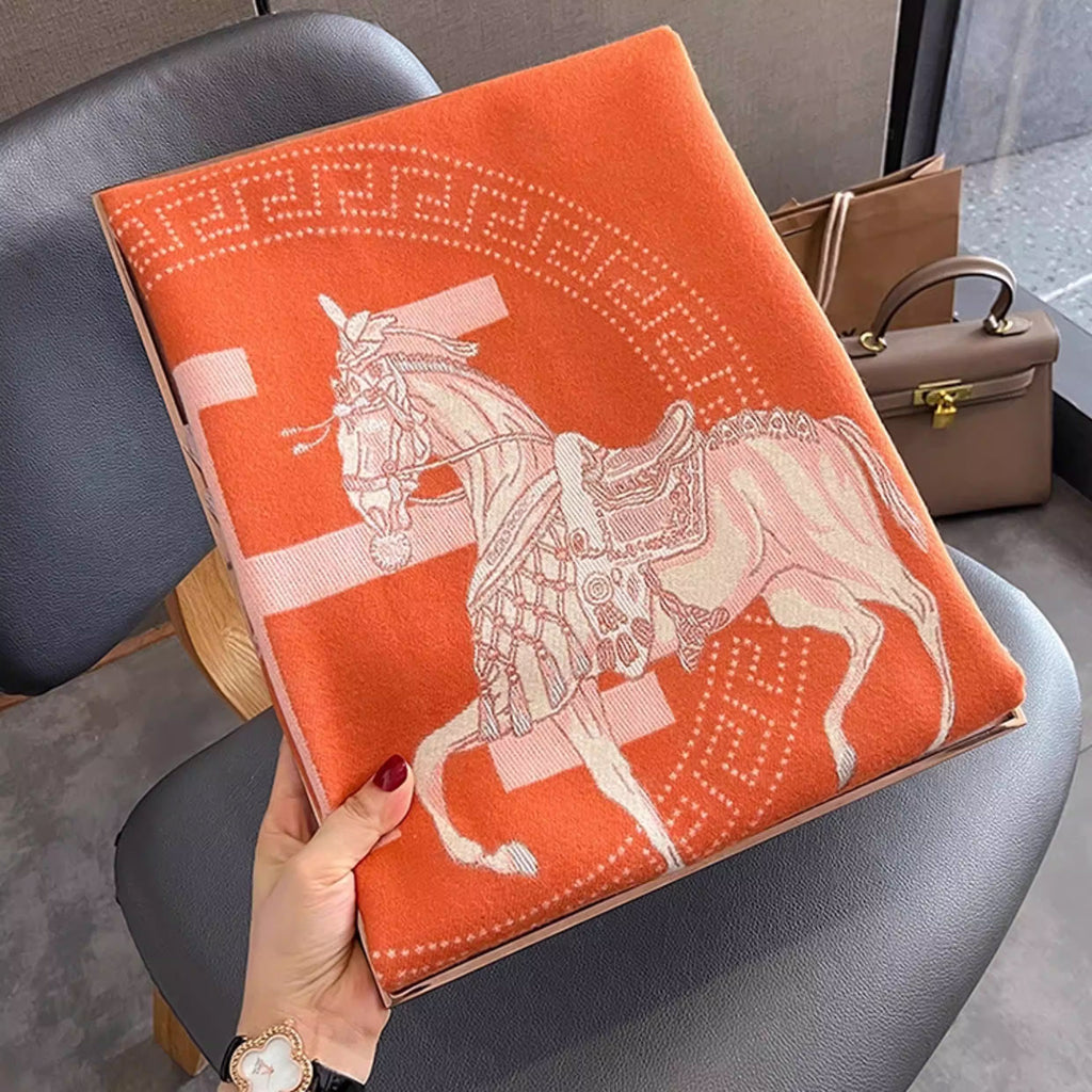 Folded orange large winter scarf with ivory letter, the cashmere-feel fabric showing a clear horse pattern 