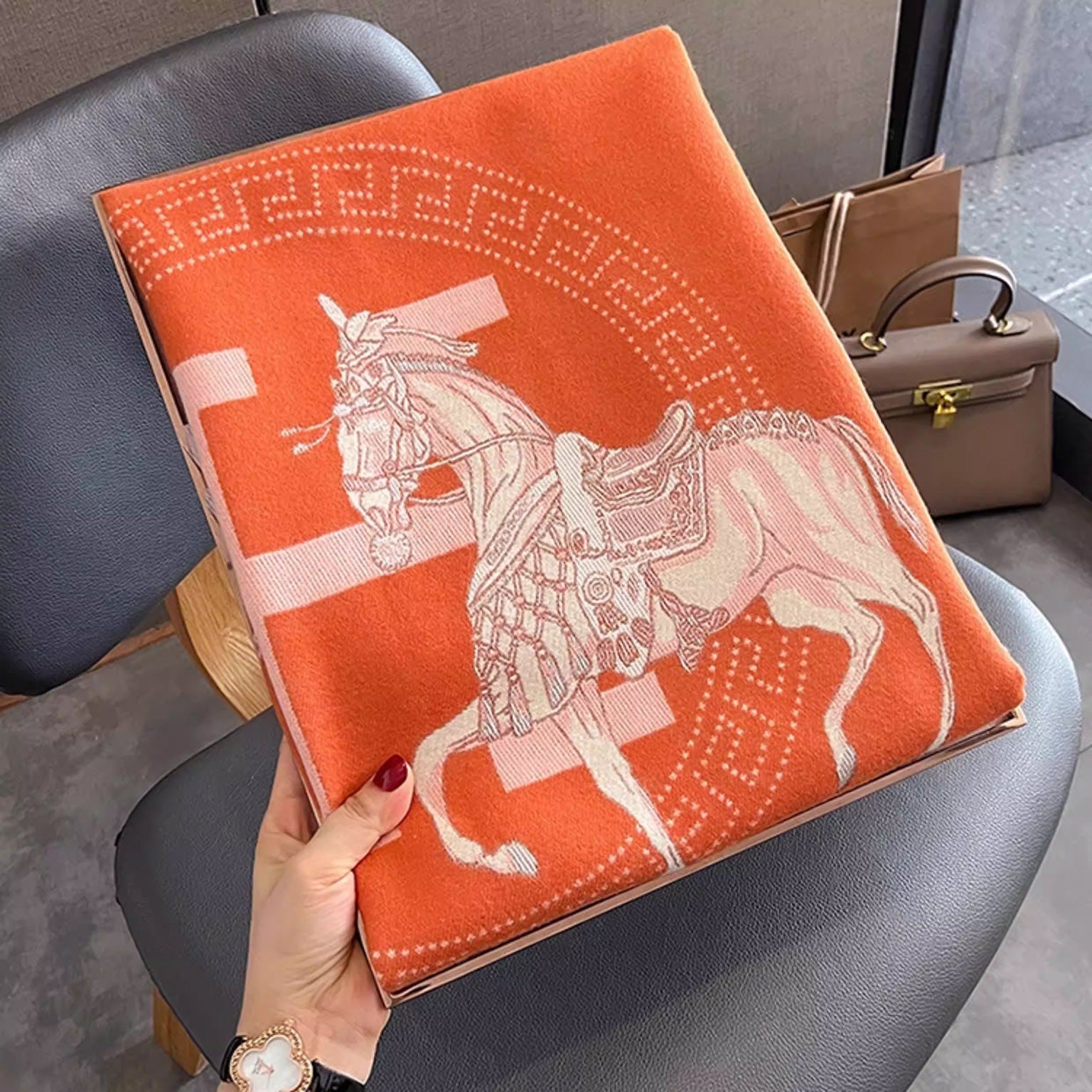 Folded orange large winter scarf with ivory letter, the cashmere-feel fabric showing a clear horse pattern 